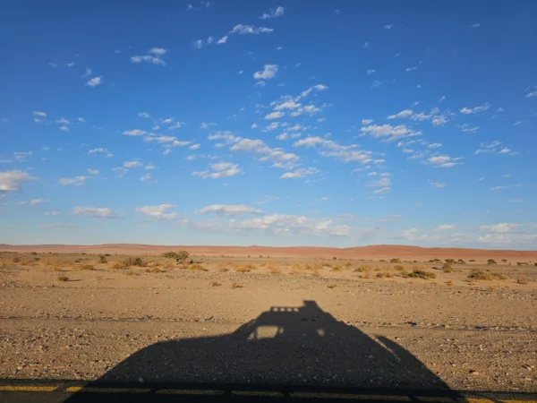 Sombra del coche 4x4 en una carretera de Namibia con las nubes y las dunas al fondo